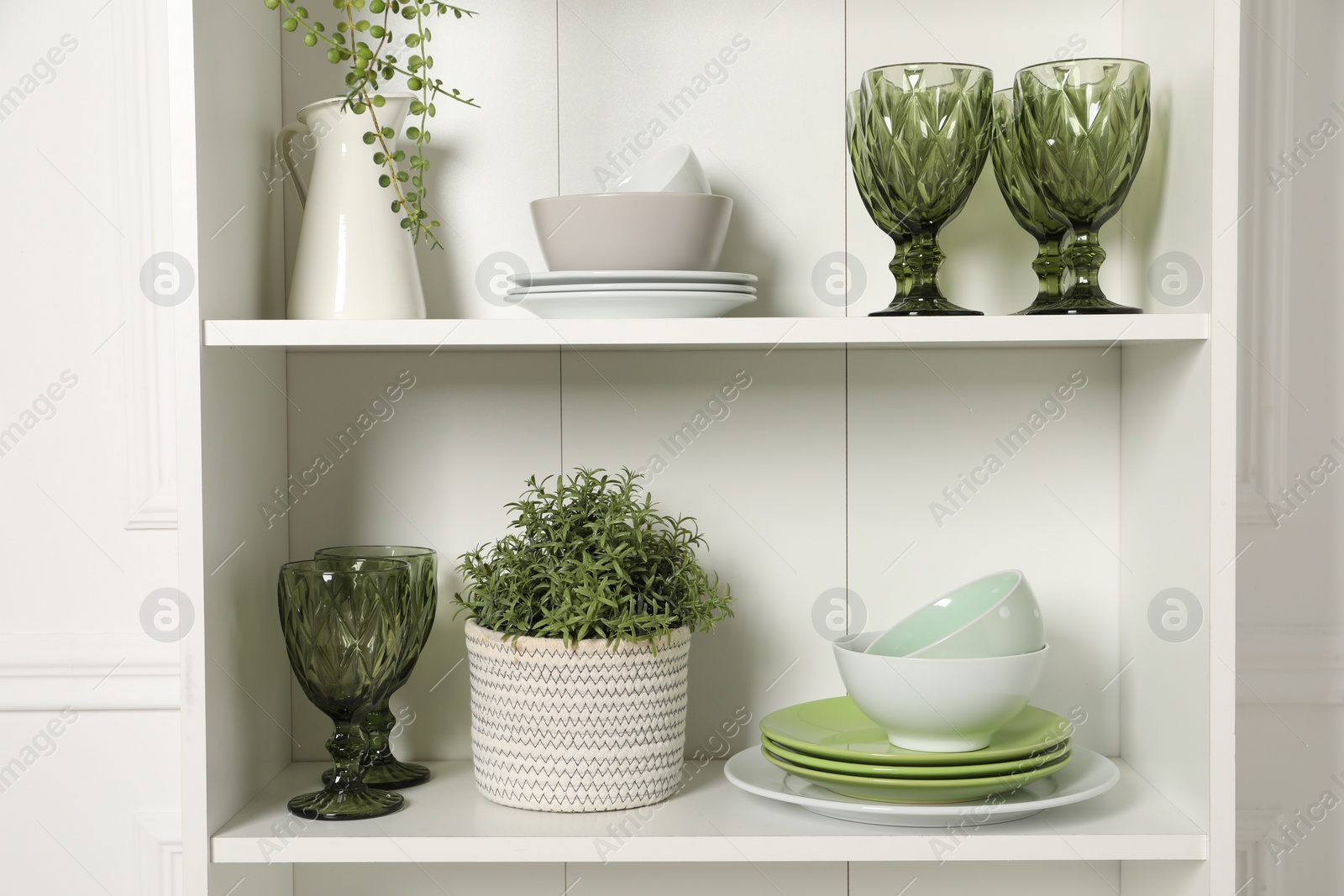 Photo of Different clean dishware and houseplant on shelves in cabinet indoors