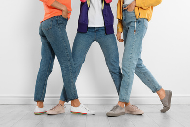 Photo of Group of young women in stylish jeans near white wall, closeup