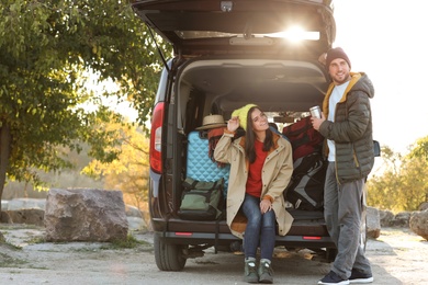 Photo of Young couple packing camping equipment into car trunk outdoors
