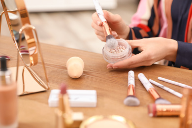 Photo of Beauty blogger with brush and highlighter at table, closeup
