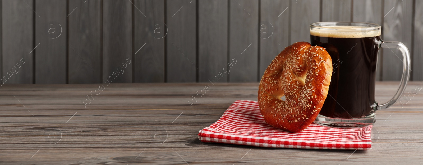 Image of Tasty pretzel and glass of beer on wooden table, space for text. Banner design