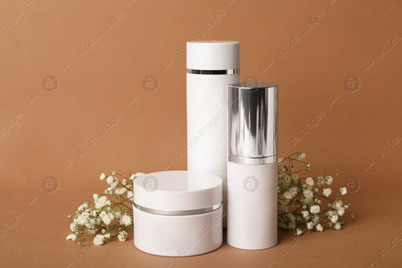 Photo of Set of luxury cosmetic products and flowers on brown background