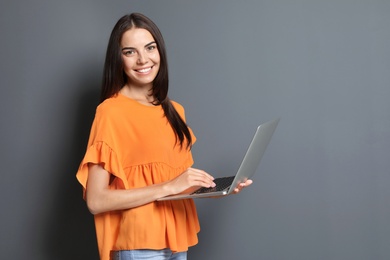 Young woman with modern laptop on grey background