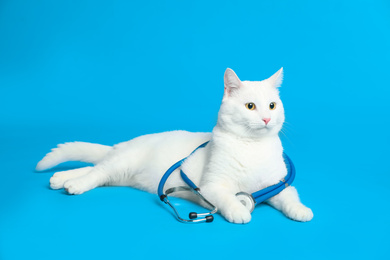 Photo of Cute cat with stethoscope as veterinarian on light blue background