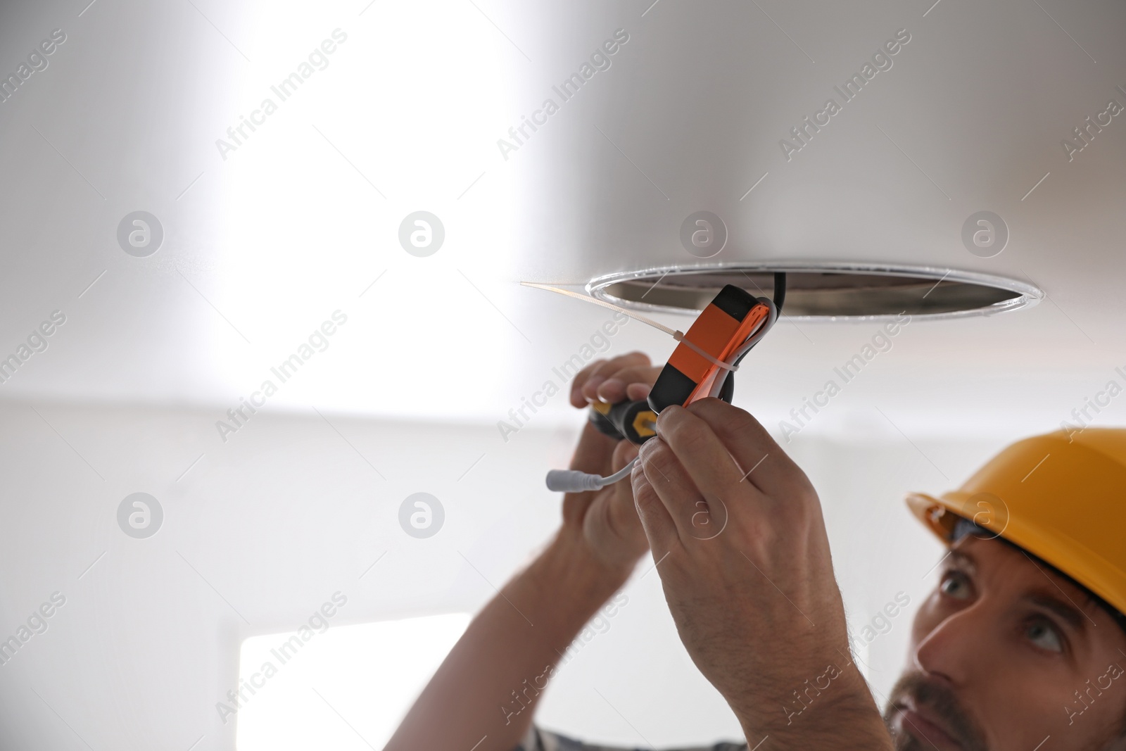 Photo of Worker repairing lamp on stretch ceiling indoors. Space for text