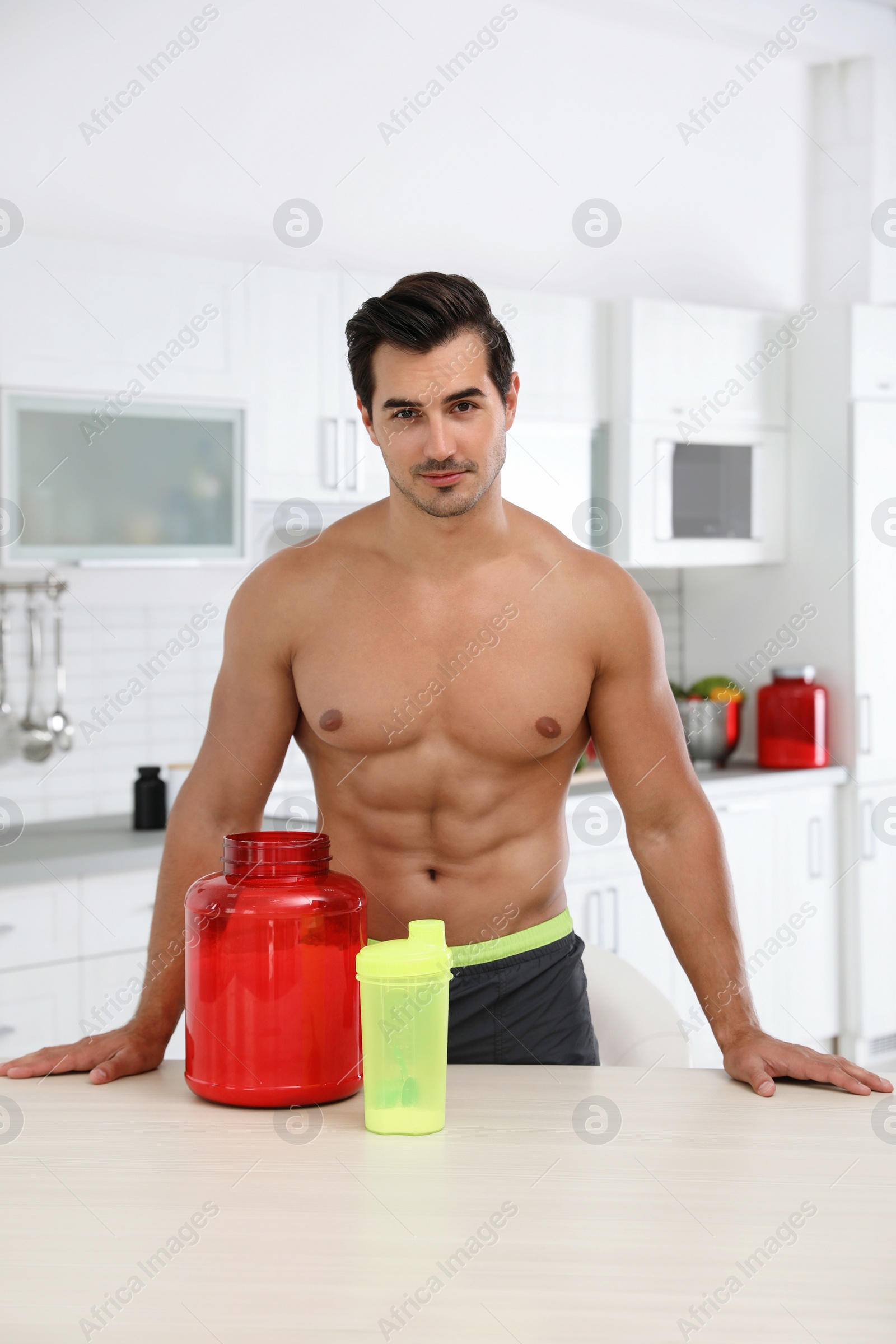 Photo of Young shirtless athletic man with protein shake powder in kitchen