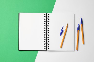 Photo of Ballpoint pens and notebook on color background, flat lay