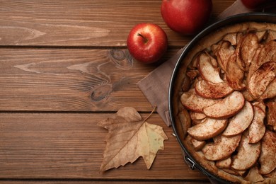 Photo of Delicious apple pie, fresh fruits and dry leaf on wooden table, flat lay. Space for text