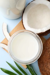 Photo of Glass of delicious vegan milk, coconuts and leaf on light blue background, flat lay