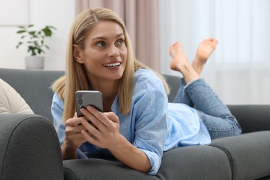 Photo of Happy woman sending message via smartphone on couch at home