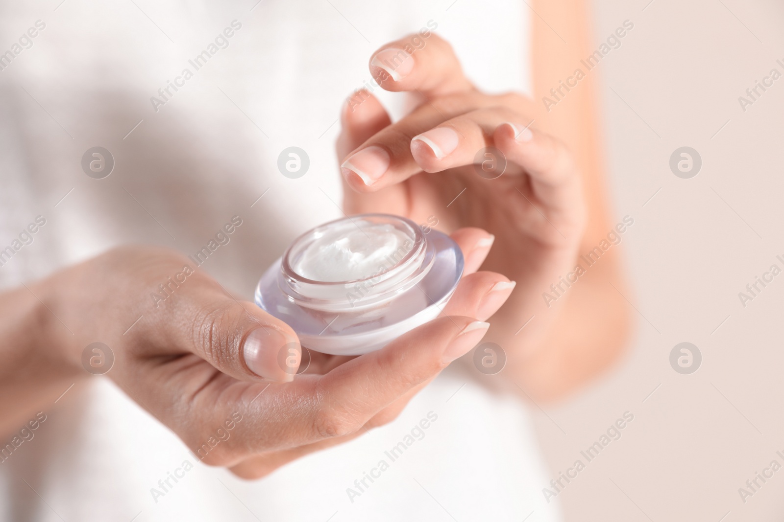 Photo of Young woman holding glass jar of cream on light background, closeup
