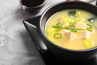 Bowl of delicious miso soup with tofu on light grey table, closeup. Space for text