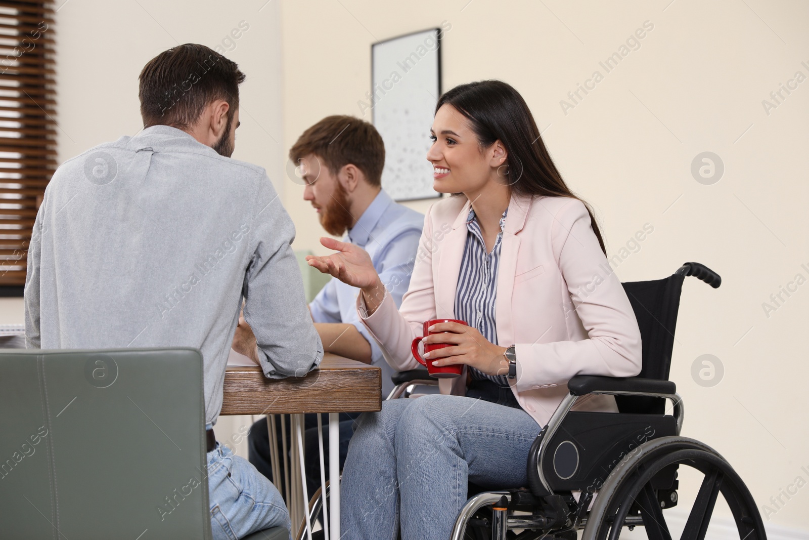 Photo of Young woman in wheelchair with colleagues at workplace