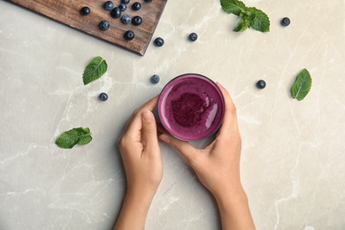 Photo of Woman holding glass of delicious acai juice on table, top view