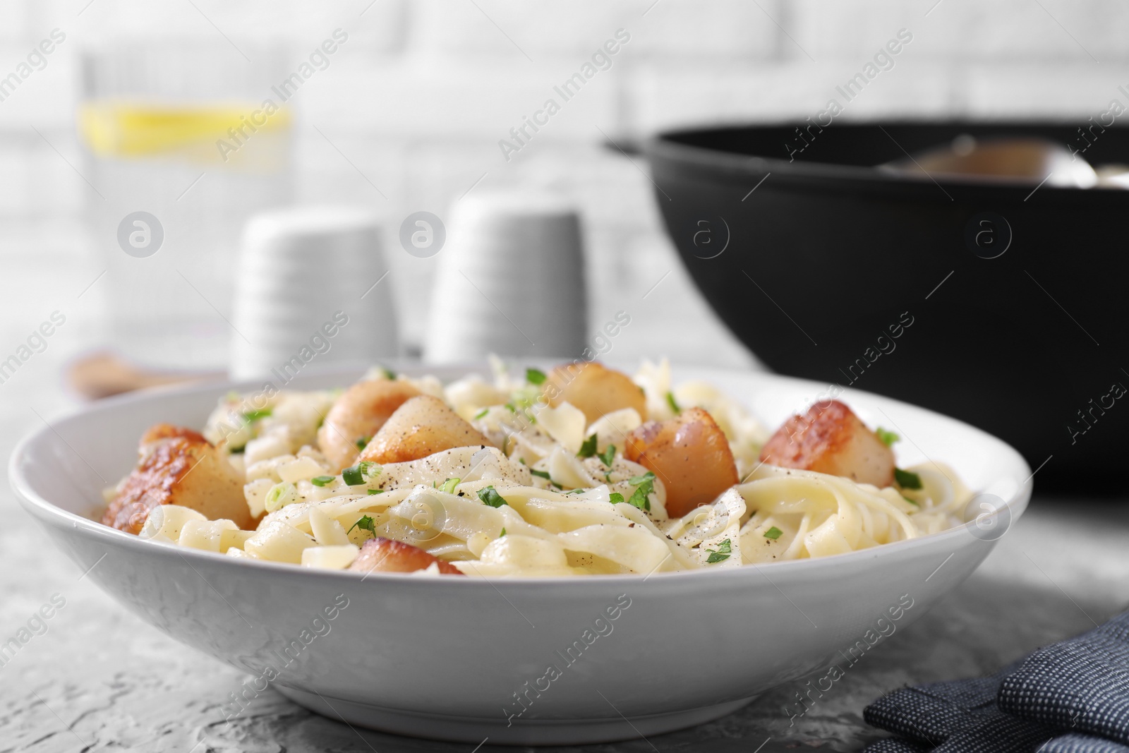 Photo of Delicious scallop pasta with spices in bowl on gray table, closeup