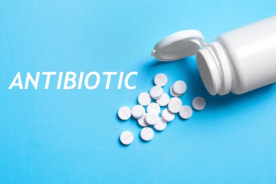 Word Antibiotic, pills and bottle on light blue background, above view