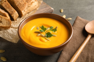 Photo of Delicious pumpkin cream soup in bowl on gray background