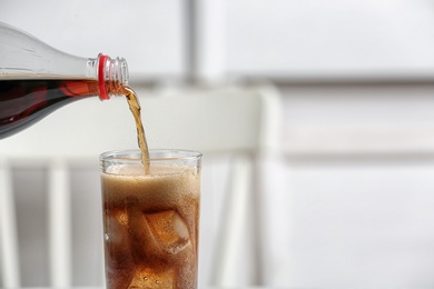 Pouring cola from bottle into glass on blurred background, closeup. Space for text