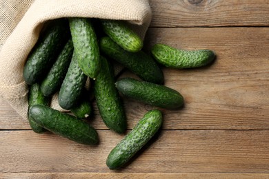 Photo of Fresh ripe cucumbers in sack on wooden table, flat lay. Space for text