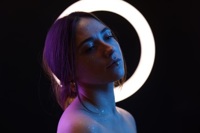 Photo of Beautiful woman and ring lamp on dark background in neon lights