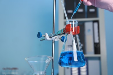 Laboratory analysis. Woman dripping blue liquid into flask on stand indoors, closeup. Space for text