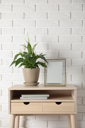 Spathiphyllum plant in pot and photo frame on table near brick wall, space for text. Home decor