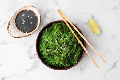 Photo of Tasty seaweed salad in bowl served on white marble table, flat lay
