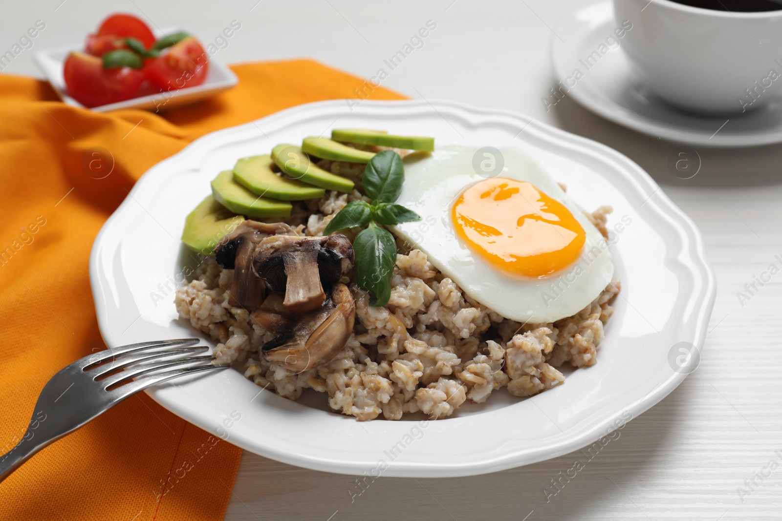 Photo of Tasty boiled oatmeal with fried egg, avocado and mushrooms served on white wooden table