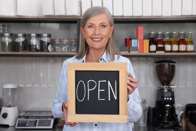 Photo of Happy business owner holding open sign in her coffee shop