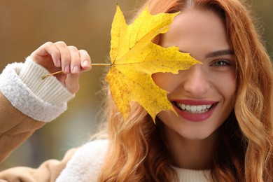 Photo of Portrait of smiling woman covering eye with autumn leaf outdoors, closeup