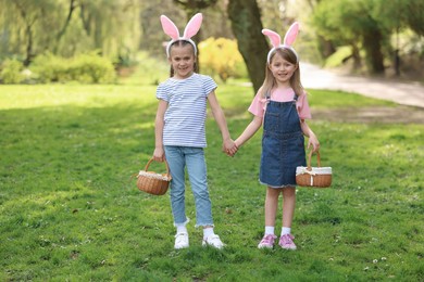 Photo of Easter celebration. Cute little girls with bunny ears holding wicker baskets outdoors