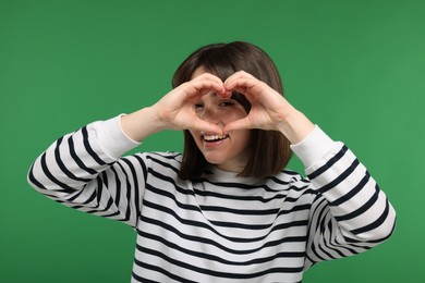 Photo of Happy woman looking through folded in shape of heart hands on green background