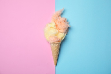 Photo of Ice cream cone with fluffy cotton candy on color background, top view