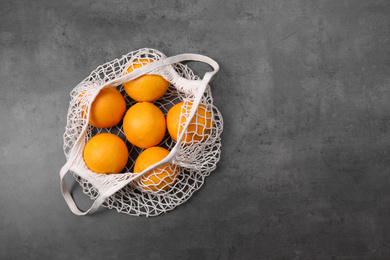 Photo of Net bag with oranges on grey table, top view. Space for text