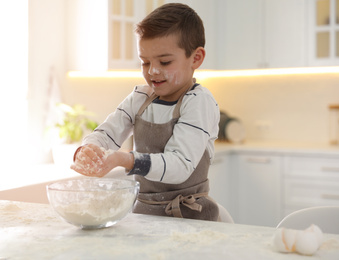 Photo of Cute little boy cooking dough at table in kitchen