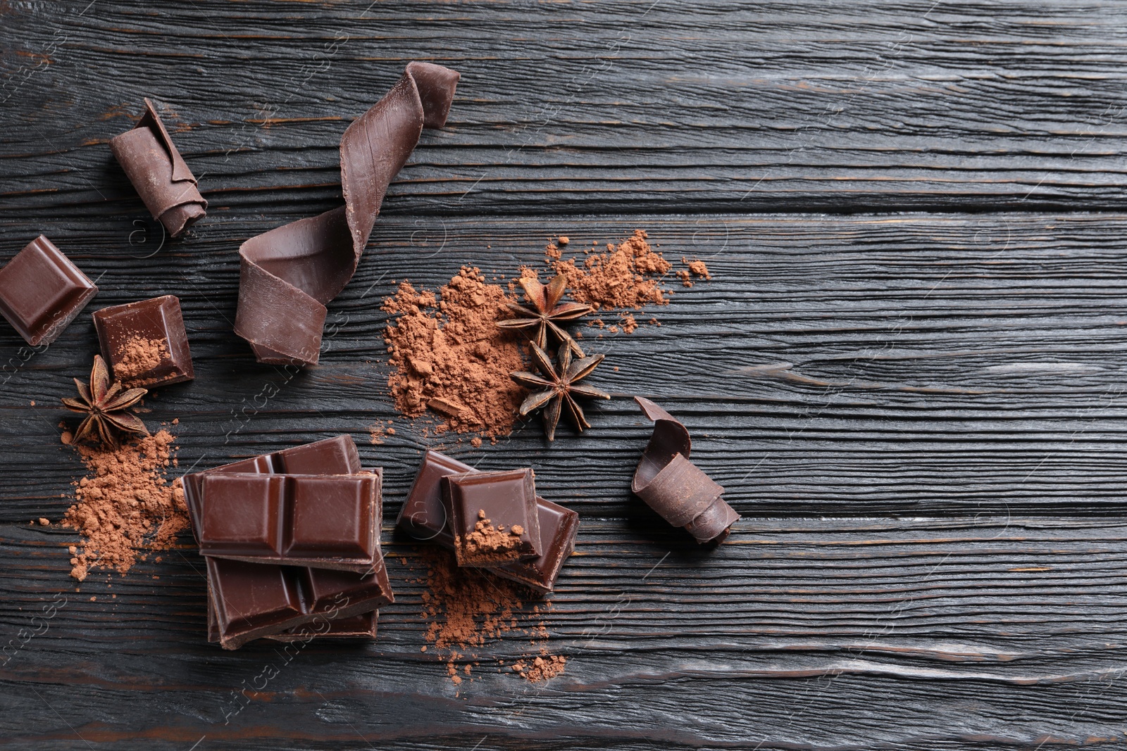 Photo of Pieces of black chocolate on wooden table, flat lay. Space for text