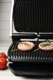 Electric grill with homemade sausages, rosemary and tomatoes on wooden table