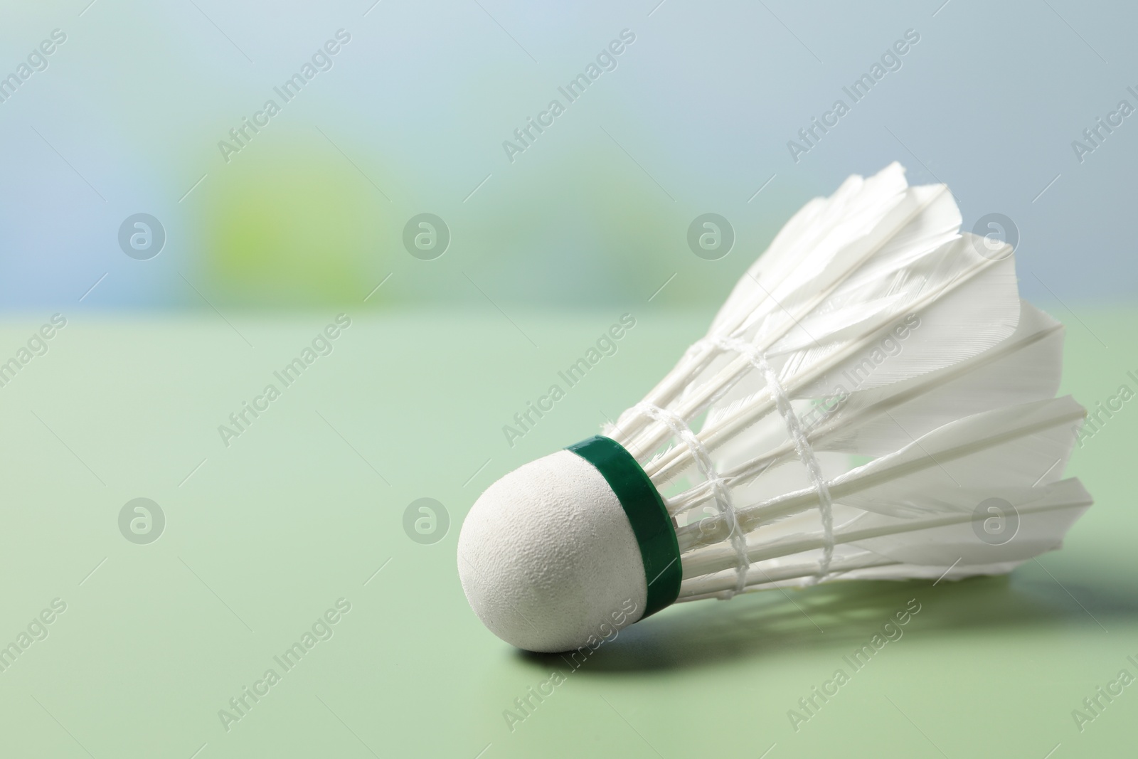 Photo of Feather badminton shuttlecock on green table against blurred background, closeup. Space for text