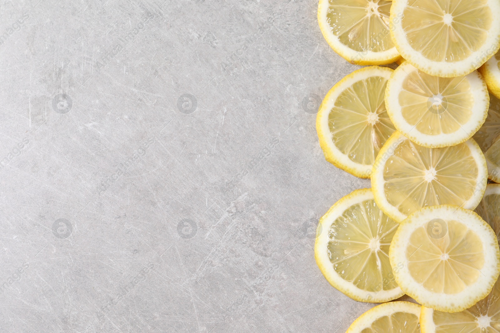 Photo of Slices of fresh lemons on grey table, top view. Space for text