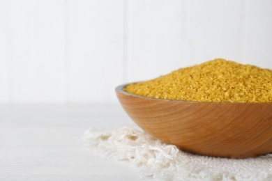 Napkin and bowl with uncooked bulgur on white wooden table, closeup. Space for text