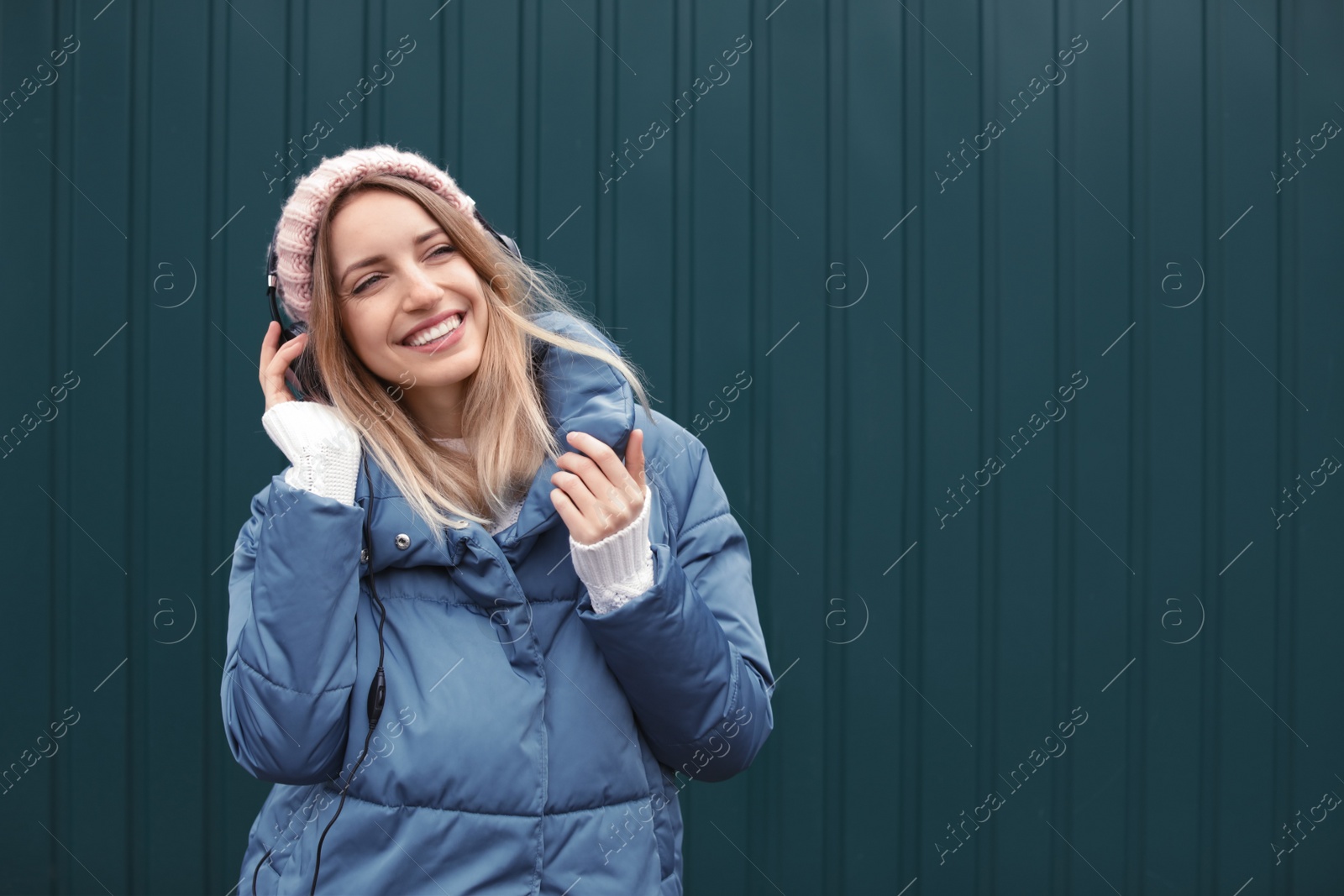 Photo of Young woman with headphones listening to music near color wall. Space for text