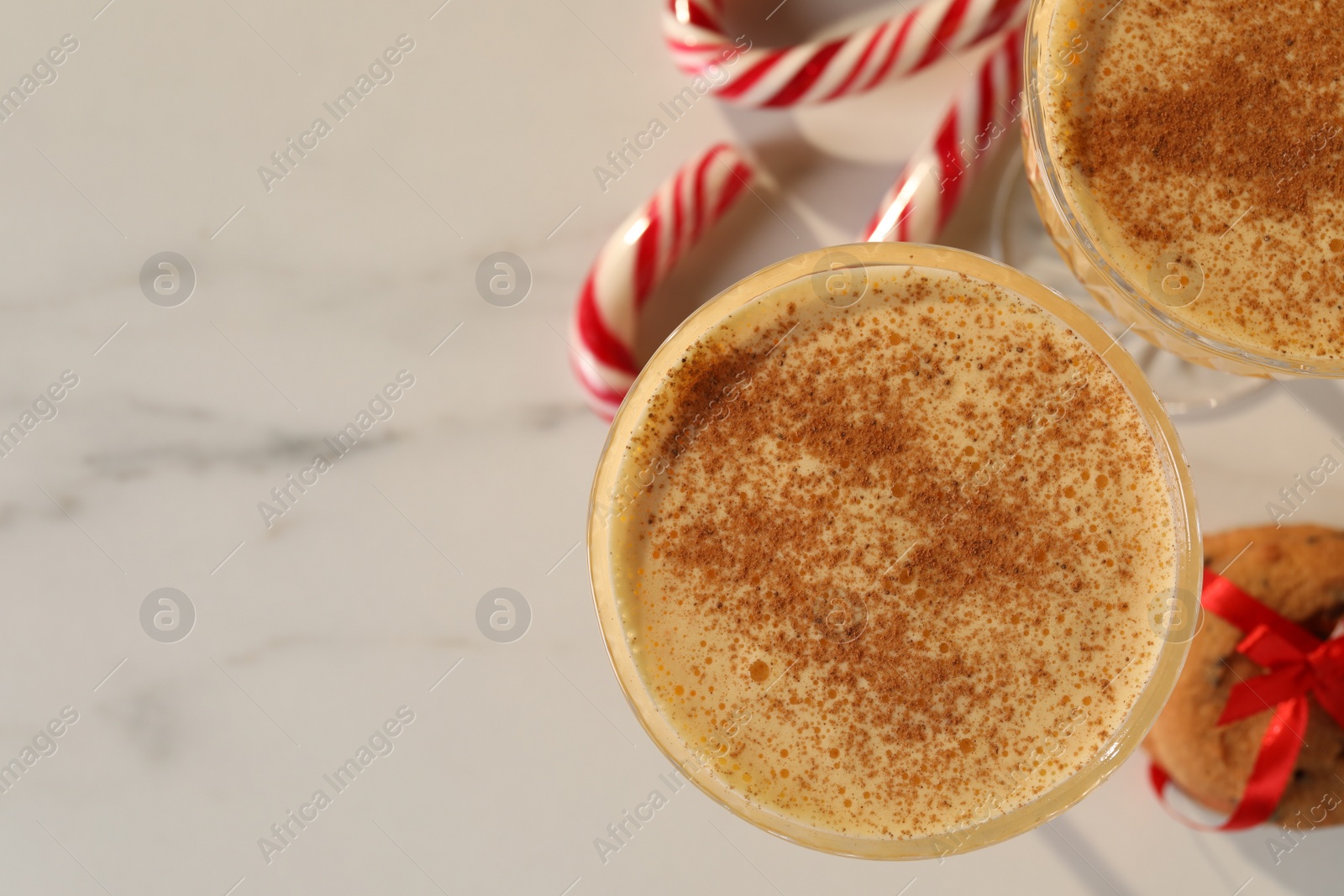 Photo of Tasty eggnog with cinnamon. cookies and candy canes on white marble table, flat lay. Space for text