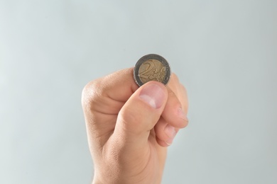 Young man holding coin on grey background, closeup