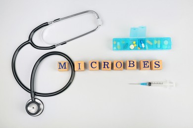 Photo of Word Microbes made with wooden cubes, pills and stethoscope on white background, flat lay
