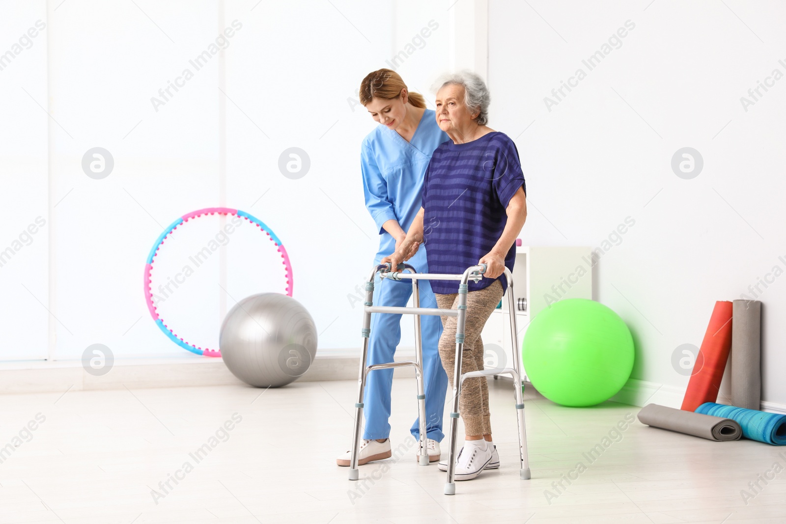 Photo of Caretaker helping elderly woman with walking frame indoors