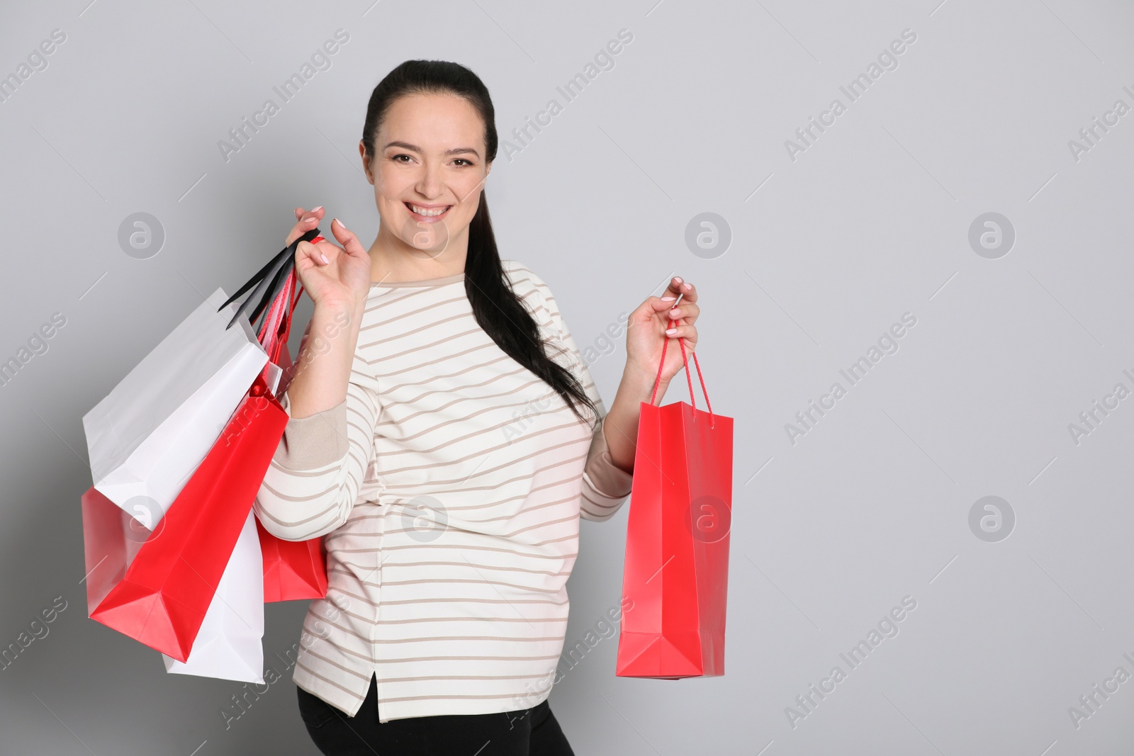 Photo of Beautiful overweight woman with shopping bags on light grey background. Space for text