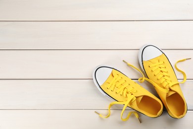 Pair of yellow sneakers on white wooden table, flat lay. Space for text