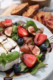 Delicious salad with brie cheese, prosciutto, berries and balsamic vinegar on plate, closeup