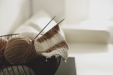 Yarn balls and knitting needles in metal basket on table indoors, space for text. Creative hobby