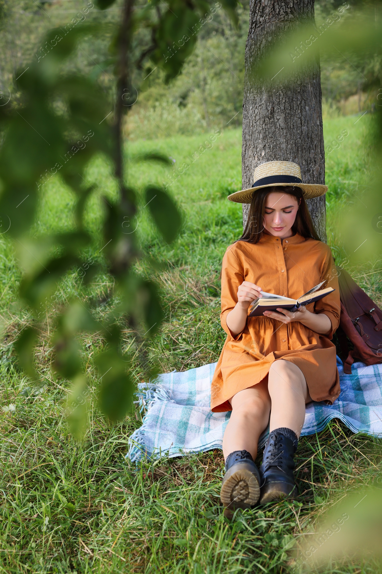 Photo of Young woman reading book under tree on meadow